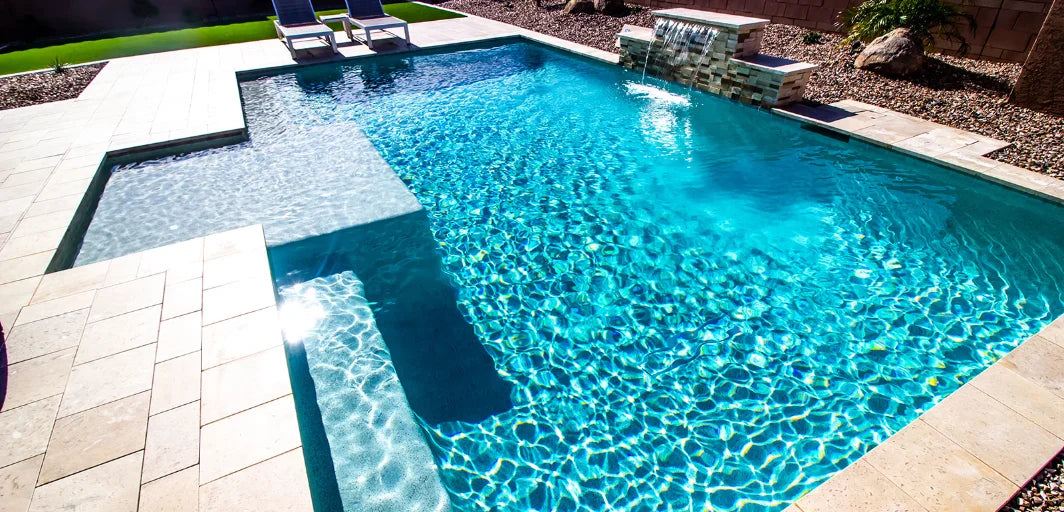 Turkos pool med inbyggd vattenfall och ljusa stenplattor runt kanten.