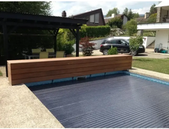 AquaTop-bassengtrekk med opprulling over vannflaten – 60 x 14 mm, mørkeblå ribbet overflate, trebenk ved siden av