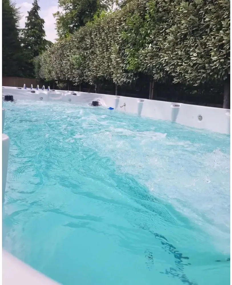 Vit PassionSpa Spirit Swim Spa med turkost vatten och jetstrålar omgiven av gröna träd