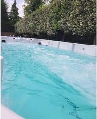 Vit PassionSpa Spirit Swim Spa med turkost vatten och jetstrålar omgiven av gröna träd