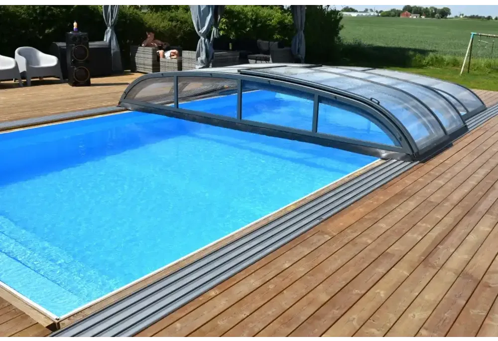 Blå inground pool med Pooltak Nivo Kit 650B transparenta paneler på trädeck. Installation finns