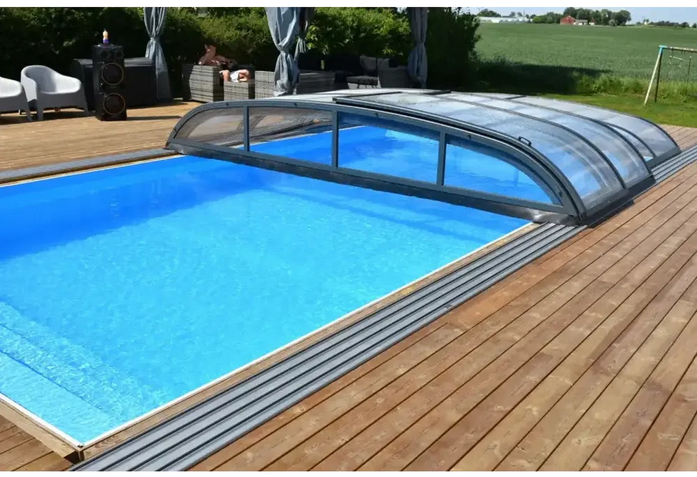 Blå inground pool med Pooltak Nivo Kit 650B transparenta paneler på trädeck. Installation finns
