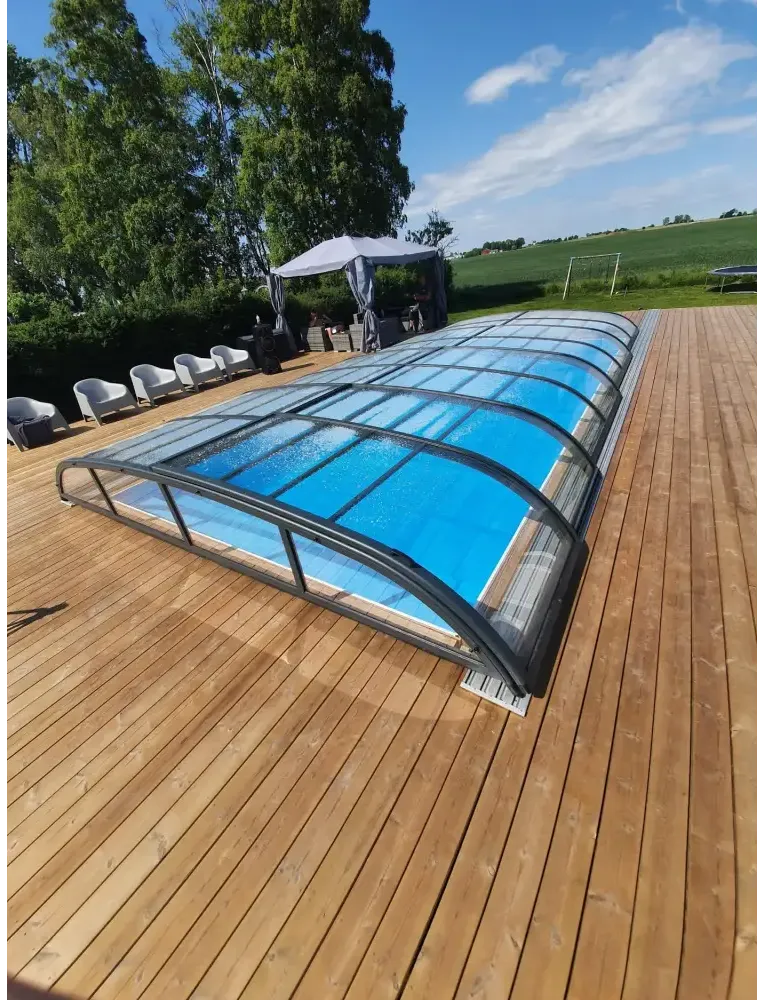 Pooltak Nivo Kit 860B med blå pool, kurvad glasöverdel och svart ram på trädeck