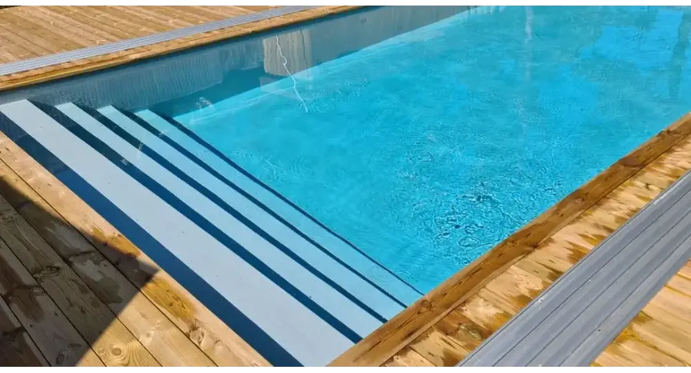 Pooltime Exklusiv 12mm rektangulär pool med klart blått vatten, trädeck och grå metalltrappor